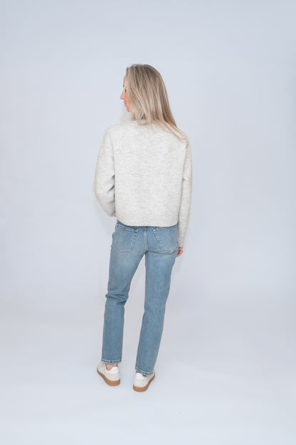 In studio photograph from behind of a woman wearing a gray cozy sweater and jeans.