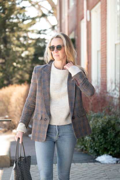 Woman dressed up in jeans and a blazer adjusting the collar of her cozy sweater while walking.